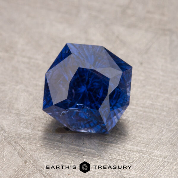 1.73-Carat Ceylon Sapphire A 1.73-carat Ceylon sapphire with a geometric shape is placed on a textured surface. The text "Earth's Treasure" is below the gemstone.