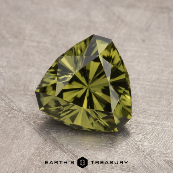 1.77-Carat Australian Sapphire (Heated) A 1.77-carat Australian sapphire, heated and faceted in a triangular shape, is placed on a textured metallic surface. The gem is labeled "Earth's Treasury.