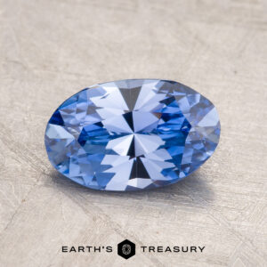 A 1.57-carat Ceylon Sapphire, expertly faceted into an oval shape, is displayed against a textured gray background with the "EARTH'S TREASURY" logo prominently positioned at the bottom center.