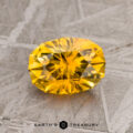 A 1.73-carat golden yellow Montana sapphire (heated) showcased on a textured gray surface, with the text "EARTH'S TREASURY" beneath.