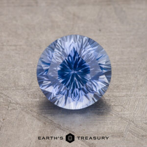 A close-up image of a round brilliant-cut blue gemstone on a textured surface with the text "1.99-Carat Ceylon Sapphire" at the bottom.