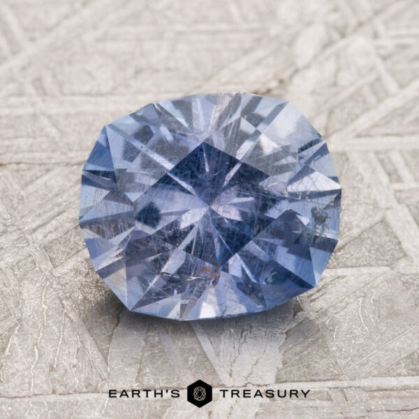 2.53-Carat Bluish Violet Umba Sapphire A 2.53-carat Violet-Blue Umba Sapphire, with intricate faceting, is placed against a textured light grey background, with the text "EARTH'S TREASURY" at the bottom center.