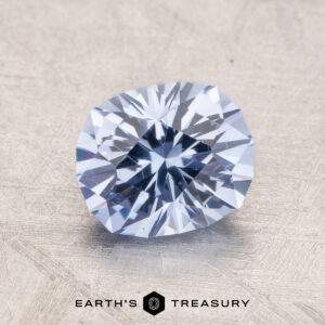 A close-up of a faceted pale violet-blue 2.48-Carat Ceylon Sapphire gemstone on a textured surface with the text "Earth's Treasury" at the bottom.