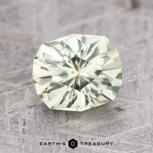 2.15-Carat Light Yellow Montana Sapphire (Heated) A 2.15-carat light yellow Montana sapphire (heated) is placed on a textured surface. The gem has a brilliant cut and a geometric pattern. The bottom of the image features the text "Earth's Treasury" alongside a hexagonal icon.