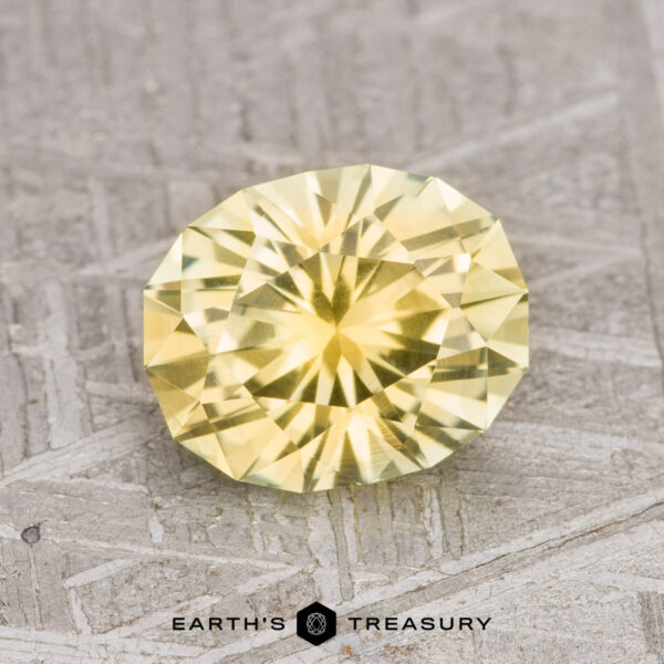 2.13-Carat Light Yellow Montana Sapphire (Heated) A round, faceted 2.13-carat light yellow Montana sapphire (heated) is placed on a textured grey surface. The text "EARTH'S TREASURY" is written below the gemstone.