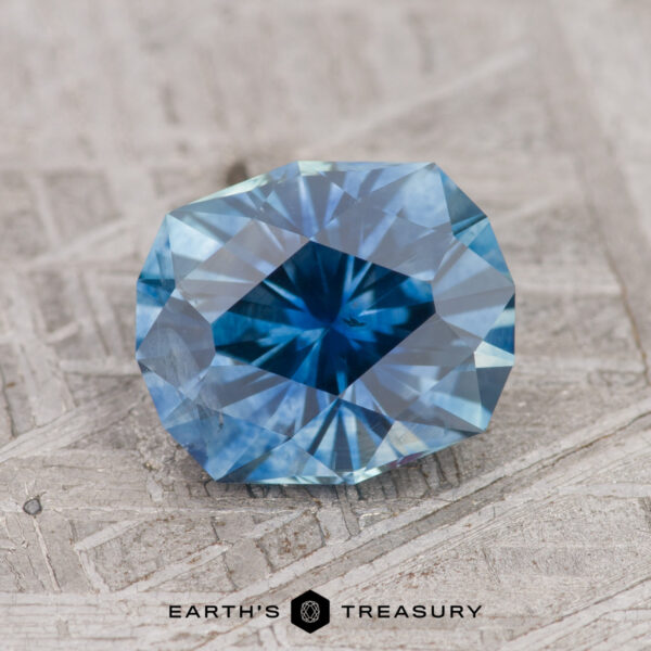 2.10-Carat Teal Blue Montana Sapphire (Heated) A faceted teal blue Montana sapphire, weighing 2.10 carats and displayed on a textured surface, with the text "EARTH'S TREASURY" visible at the bottom.