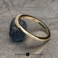 The "Paloma" band in 14k yellow gold is shown leaning against a rough blue gemstone on a textured gray surface, with the Earth's Treasury logo beneath.