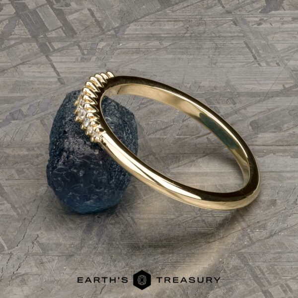 The "Paloma" band in 14k yellow gold The "Paloma" band in 14k yellow gold is shown leaning against a rough blue gemstone on a textured gray surface, with the Earth's Treasury logo beneath.