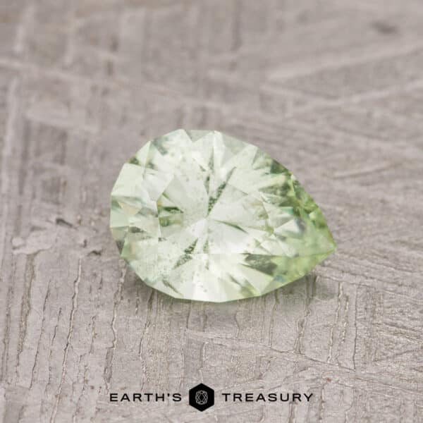 0.80-Carat Pale Kiwi Green Grossular Garnet The 0.80-carat pale kiwi green grossular garnet, featuring a faceted pear shape, rests on a textured surface.