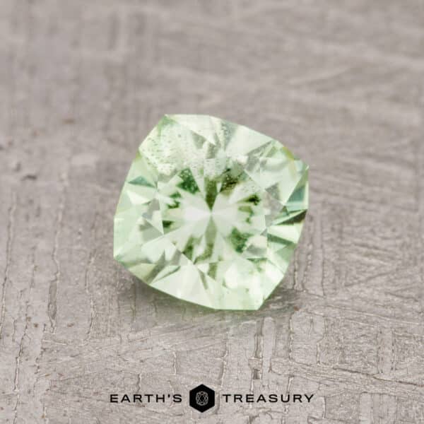 0.71-Carat Mint Green Garnet A 0.71-carat mint green garnet with intricate faceting, showcased on a textured gray background. Text reads "Earth's Treasury" at the bottom of the image.