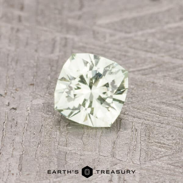 0.47-Carat Pale Kiwi Green Grossular Garnet A cushion-cut pale kiwi-green gemstone, weighing 0.47 carats, resting on a textured gray surface with the "Earth's Treasury" logo at the bottom.