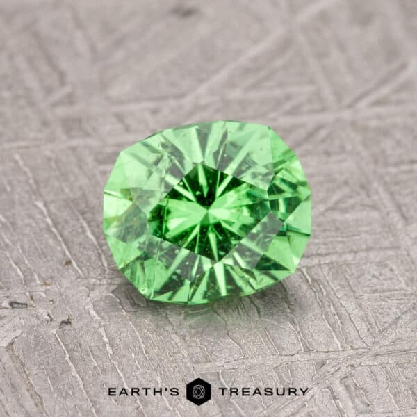 0.99-Carat Tsavorite Garnet A faceted green gemstone on a textured surface, labeled "0.99-Carat Tsavorite Garnet.