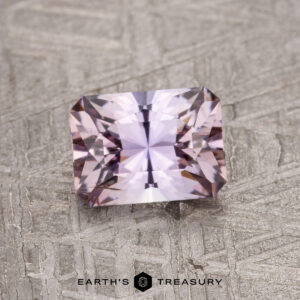 A faceted, rectangular 0.91-carat Fancy Tanzanite gemstone displayed on a textured gray surface labeled "Earth's Treasury.