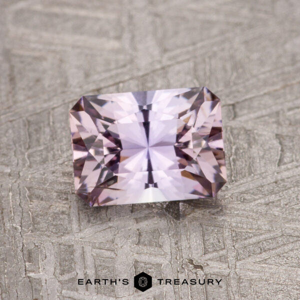 0.91-Carat Unheated Tanzanite (Zoisite) A faceted, rectangular 0.91-carat Fancy Tanzanite gemstone displayed on a textured gray surface labeled "Earth's Treasury.
