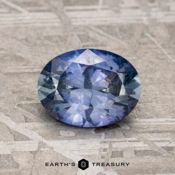 1.37-Carat Steel-Blue Umba Sapphire An oval faceted 1.37-carat steel-blue Umba sapphire gemstone, set on a textured stone background, with the text "Earth's Treasury" displayed at the bottom.