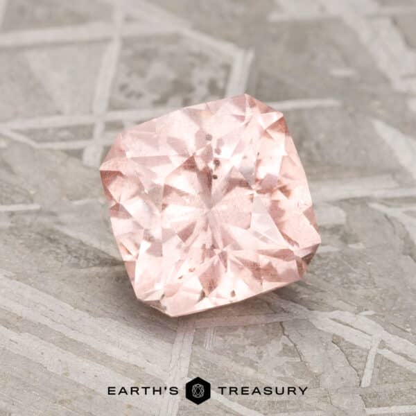 1.84-Carat Pink-Peach Pastel Pyrope Garnet A 1.84-carat pink-peach pastel pyrope garnet is showcased on a textured gray surface, with the text "Earth's Treasury" at the bottom.