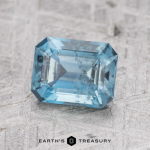 A 1.31-carat Nasarawa Teal Aqua gemstone with an emerald cut showcased on a textured gray surface.