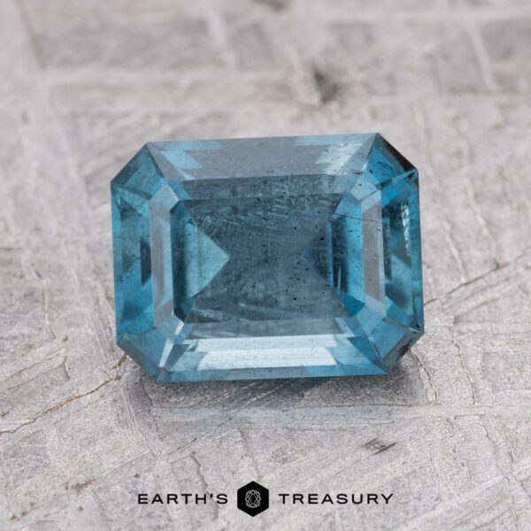 1.59-Carat Nasarawa Teal Aqua A rectangular, teal aqua gemstone with step-cut facets is placed on a textured gray surface. The text "1.59-Carat Nasarawa" appears below the gem.