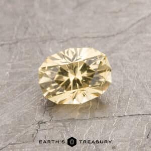 ET1060, a yellow faceted gemstone resting on a textured gray surface, with "Earth's Treasury" inscribed below.