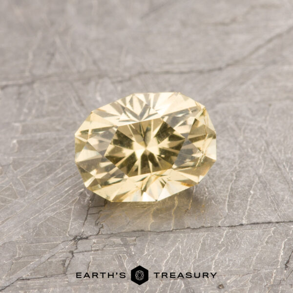 ET1060 ET1060, a yellow faceted gemstone resting on a textured gray surface, with "Earth's Treasury" inscribed below.