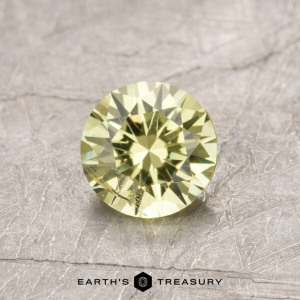 ET1090 A faceted green gemstone, product ET1090, displayed on a textured gray surface.