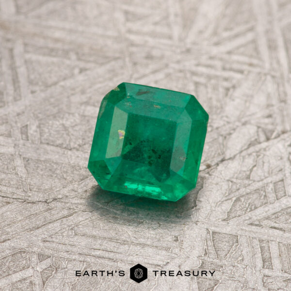0.54-Carat Rich Green Colombian Emerald (Oiled) A textured surface showcases a green emerald cut gemstone, with "Earth's Treasury" inscribed below.