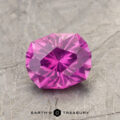 A pink ET1123 gemstone with a geometric cut, displayed on a textured gray surface.