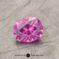 Product ET1127, a faceted gemstone with a purple-pink hue and an intricate cut, is situated on a textured gray surface, showcasing the Earth's Treasury logo beneath it.