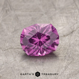 A faceted pink gemstone, product ET1128, rests on a textured gray surface labeled "Earth's Treasury.