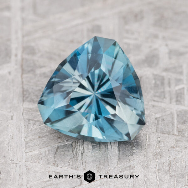 1.50-Carat Nasarawa Teal Aqua A 1.50-carat Nasarawa Teal Aqua gemstone, with intricate facets and a triangular cut, is displayed on a textured surface.