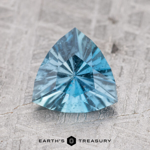 1.11-Carat Nasarawa Teal Aqua A 1.11-carat Nasarawa teal aqua trillion-cut gemstone with visible facets, displayed on a textured surface.