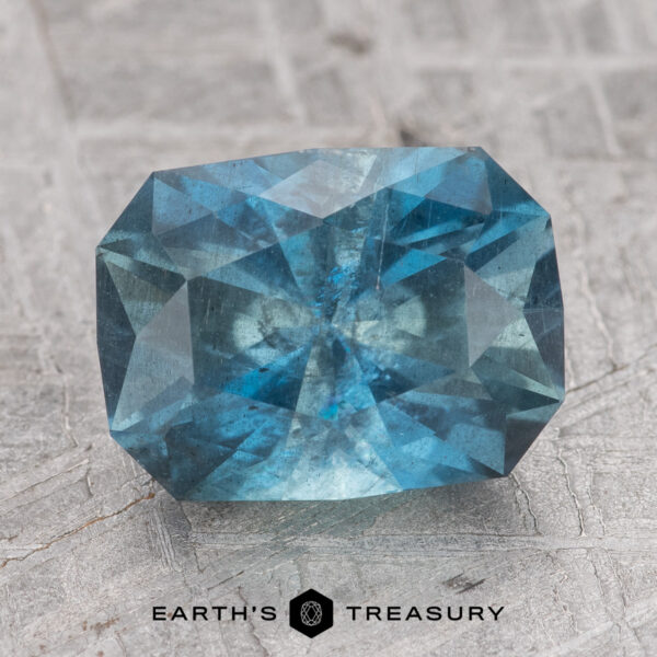 2.63-Carat Nasarawa Teal Aqua The 2.63-Carat Nasarawa Teal Aqua sapphire, with its rectangular shape and slightly rounded corners, is showcased on a textured gray surface.