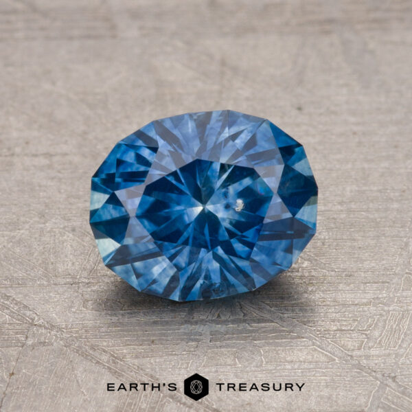 1.45-Carat Montana Sapphire (Heated) A faceted blue 1.45-carat Montana sapphire (heated) resting on a textured surface, with a logo reading "Earth's Treasury" at the bottom.