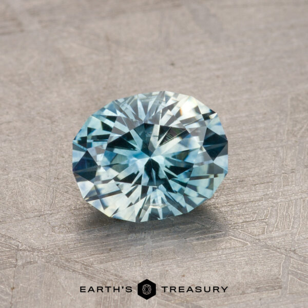 1.17-Carat Montana Sapphire (Heated) Close-up image of a round-cut blue 1.17-carat heated Montana sapphire displayed on a textured metallic surface. Text reads "Earth's Treasury" at the bottom.