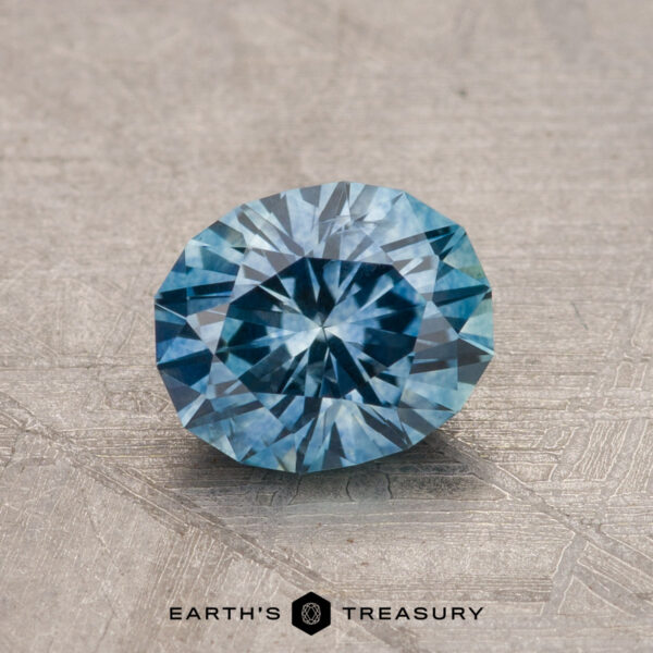 1.15-Carat Montana Sapphire (Heated) A 1.15-carat heated Montana sapphire with intricate facets lies on a textured surface, showcasing a sparkling pattern.