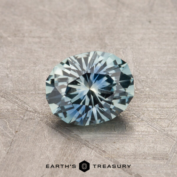 1.00-Carat Montana Sapphire (Heated) A faceted blue 1.00-carat Montana Sapphire (heated) is displayed on a textured surface with the text "Earth's Treasury" at the bottom.