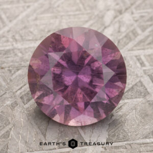 A 3.25-carat magenta purple Umba sapphire resting on a textured surface with the "Earth's Treasury" logo beneath it.