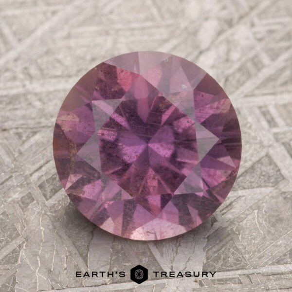 3.25-Carat Magenta Purple Umba Sapphire A 3.25-carat magenta purple Umba sapphire resting on a textured surface with the "Earth's Treasury" logo beneath it.