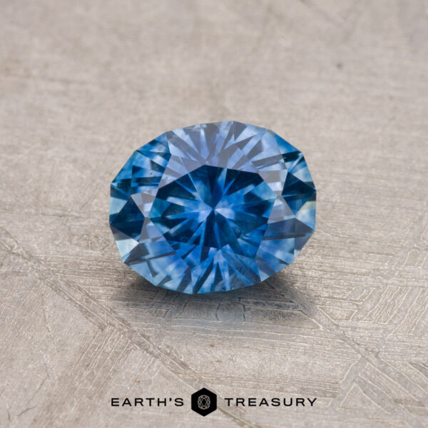 0.92-Carat Montana Sapphire (Heated) A 0.92-carat Montana Sapphire, heated and faceted in blue, displayed on a textured surface with the "Earth's Treasury" logo at the bottom.