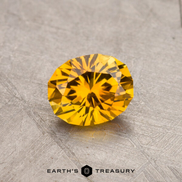 0.86-Carat Montana Sapphire (Heated) A round, faceted yellow 0.86-carat Montana sapphire (heated) displayed on a textured surface.