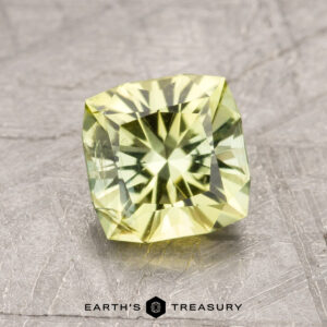 The ET1429, a cushion-cut yellow-green gemstone featuring a radiant star-like pattern, is displayed on a textured gray surface.