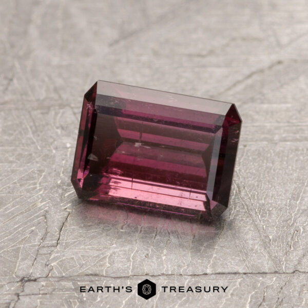 1.34-Carat Deep Raspberry Red California Tourmaline Gemstone ET1434, featuring a rectangular cut in deep pink, is showcased on a textured gray surface with the text "Earth's Treasury" below.