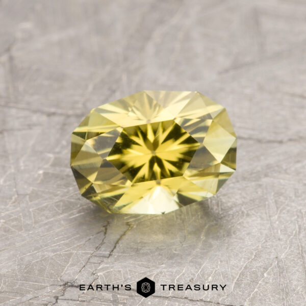 1.17-Carat Bright Yellow California Tourmaline A faceted yellow ET1445 gemstone rests on a textured gray surface, with the words "Earth's Treasury" displayed at the bottom.