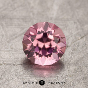 A round pink 1.35-carat California Tourmaline gemstone resting on a textured surface with the text "Earth's Treasury" beneath it.