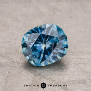 A 1.34-carat Montana Sapphire (Heated) with intricate facets rests on a textured surface, and the words "Earth's Treasury" appear at the bottom.