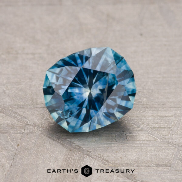 1.34-Carat Montana Sapphire (Heated) A 1.34-carat Montana Sapphire (Heated) with intricate facets rests on a textured surface, and the words "Earth's Treasury" appear at the bottom.