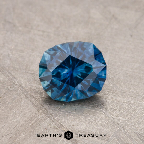 1.03-Carat Montana Sapphire (Heated) A 1.03-carat Montana sapphire, featuring a rectangular cut with multiple facets, is placed on a textured surface.