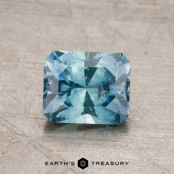 1.28-Carat Montana Sapphire (Heated) A 1.28-carat heated Montana sapphire with a radiant cut and intricate facets, displayed on a textured surface.