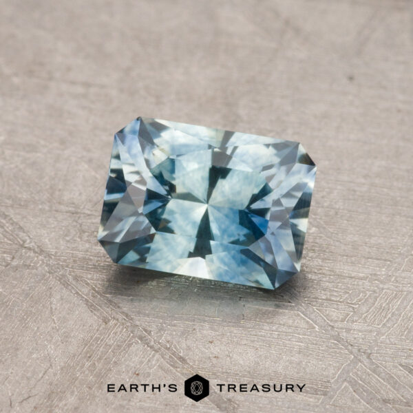 1.00-Carat Montana Sapphire (Heated) A 1.00-carat Montana sapphire (heated), featuring a rectangular, faceted design with a reflective surface, is elegantly displayed on a textured gray background.