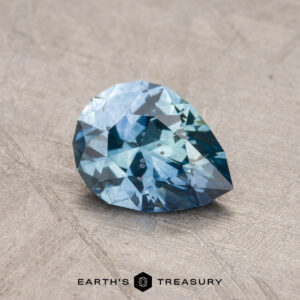 A 1.03-carat Montana sapphire, heated and pear-shaped, rests on a textured surface.
